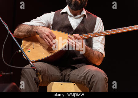 Good-looking man with a thick black beard, hands details of a musician playing a typical stringed instrument on stage, the tembur or saz Stock Photo