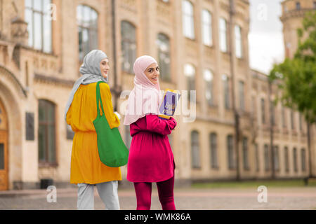 Muslim student holding books walking to classes with friend Stock Photo