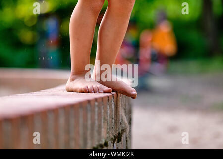 Low section of a caucasian child girl who is standing barefoot on a little stone wall with sandy feet in summer