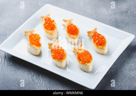 Delicious puff pastry tartlets in the shape of fish with red caviar on a festive table. Stock Photo
