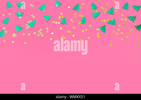 Green metallic foil christmas trees and gold stars confetti sparse on pink background. Simple holiday concept. Design template. Frame with copy space. Stock Photo