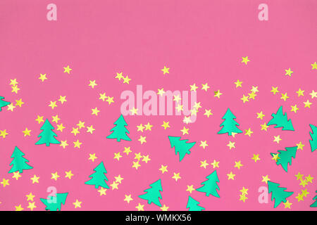 Green metallic foil christmas trees and gold stars confetti sparse on pink background. Simple holiday concept. Design template. Frame with copy space. Stock Photo