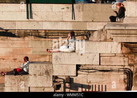Authentic travel impressions from Paris: Sun bathers on the stairs of the Seine embankments Stock Photo