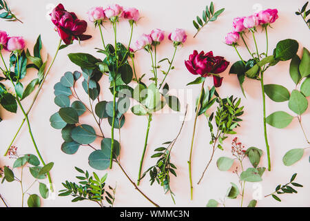 Various summer flowers flat-lay. Purple peonies, pink roses and green branches with leaves over pastel pink background, top view. Flower texture, wall Stock Photo