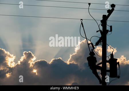 Silhouette, power lineman use clamp stick (insulated tool) to closing a transformer on energized high-voltage electric power lines. Isolated from back Stock Photo