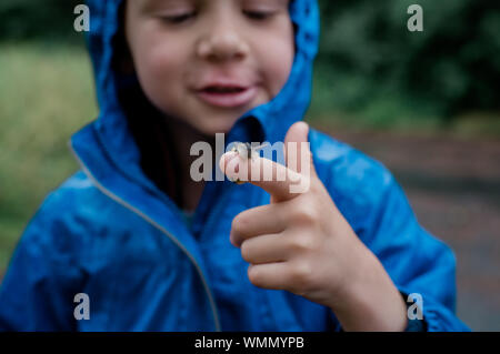 young boy standing in the rain smiling with a snail on his finger Stock Photo