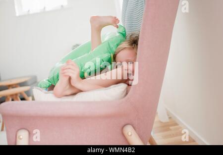 young girl sitting in a chair at home laughing playing with toys Stock Photo