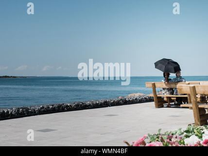 retired romantic couple sitting on bench with umbrella looking at sea Stock Photo