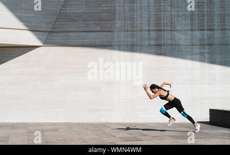 Pulled back view of female athlete running on concrete Stock Photo