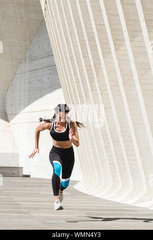 Full body of female athlete in sportswear running on concrete Stock Photo