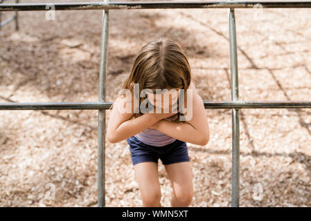 Young girl with brown hair plays on playground in summer on sunny day Stock Photo