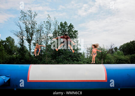 Young adult man and two children jumping on sunny day against blue sky Stock Photo