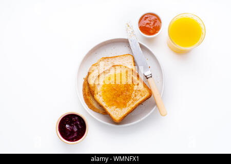 Morning toasts with butter and confiture on white table served with orange juice. Flatlay, view from above Stock Photo