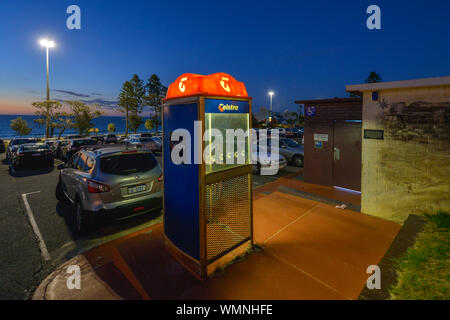 Twilight view of an illuminated Telstra telephone box in a car park, beside a beach. City Beach, Western Australia. Stock Photo