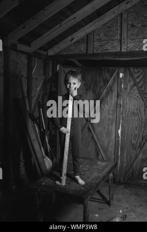 Portrait Of Boy With Yardstick On Table In Wooden Garage