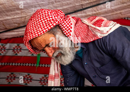 Bedouin wearing traditional Hashemite scarf pouring coffee for guests in traditional Bedouin tent. Stock Photo