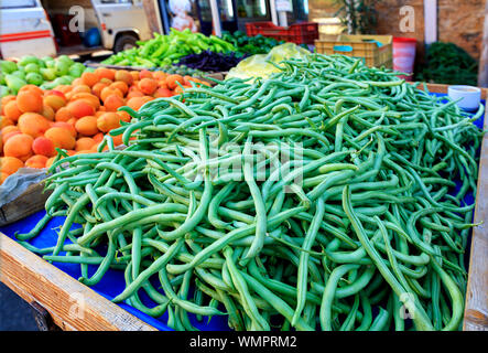 Bright background of fresh vegetables and fruits, green beans, apricots, pears, plums lying in trays in the market and attracting attention. Stock Photo