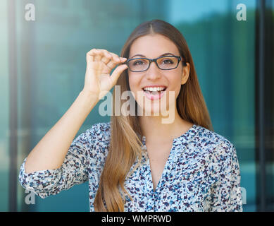 Happy beautiful young woman holds her glasses and looks at camera outdoor. Stock Photo