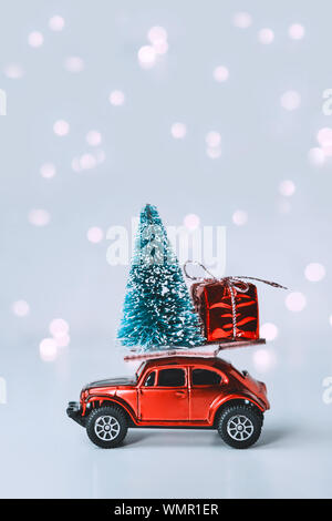 Toy car with Christmas tree and gift on roof. Background of blurred bokeh from garland. New Year and Christmas holiday concept Stock Photo
