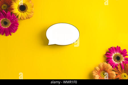 Bright beautiful gerbera flowers and bubble speech on sunny yellow background. Mother's Day, Valentine holiday. Place for text, lettering or product. Stock Photo