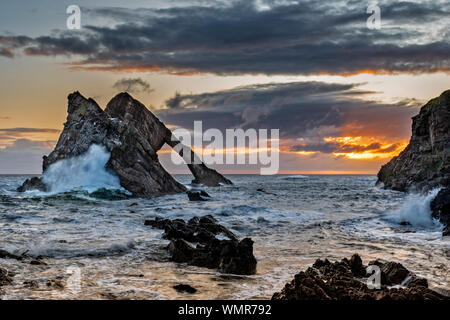 BOW FIDDLE ROCK PORTKNOCKIE MORAY SCOTLAND SUNRISE WITH STORMY SEA AND IMPRESSIVE WAVES AND SPRAY OVER THE ROCK Stock Photo