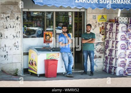 RAMALLAH, PALESTINE. August 31, 2019. Two Palestinian men stand by a grocery supermarket and look at the passerby people. Trade in Palestine, economy Stock Photo