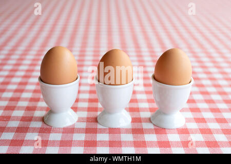 Three boiled eggs in egg cups in a row on a table Stock Photo