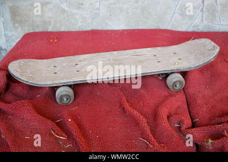 Old vintage wooden skateboard on dirty red surface, selective focus Stock Photo