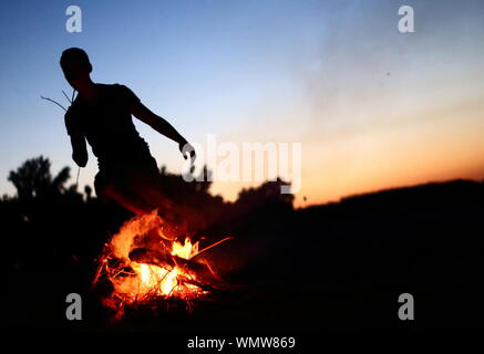 Man standing in front of campfire at dusk Stock Photo - Alamy