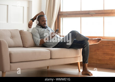 Black man relaxing on sofa at home, listen music. Stock Photo
