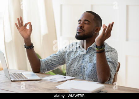 Mindful african american guy relaxing during remote working. Stock Photo