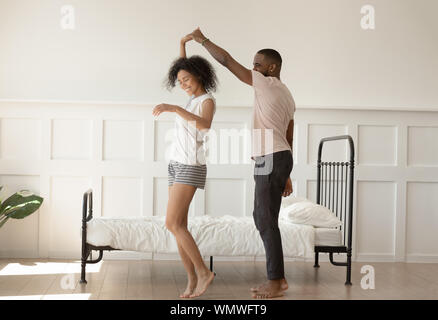 Happy barefoot african american loving family couple dancing in bedroom. Stock Photo