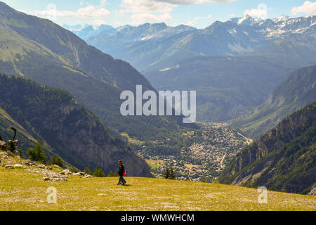 A couple of hikers walking on an Alpine meadow of the Mont Blanc massif with a panoramic view on Courmayeur valley in summer, Aosta Valley, Italy Stock Photo