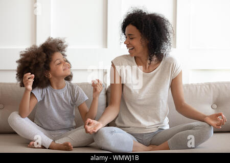 Excited african american woman practicing yoga with little daughter. Stock Photo