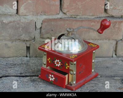 Red vintage coffee grinder on a wooden board with bricks background Stock Photo