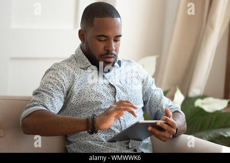 Concentrated young african american man holding digital tablet. Stock Photo
