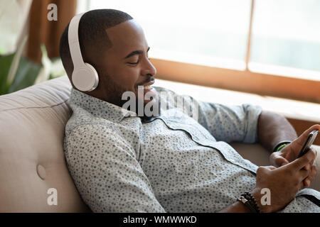 Happy african american man lying on sofa at home. Stock Photo