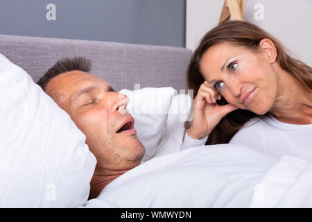 Angry Mature Woman Looking At Man Snoring In Bed At Home Stock Photo