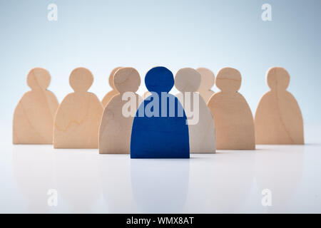 Blue Human Figure Standing In Front Of Wooden Figures Over White Desk Stock Photo