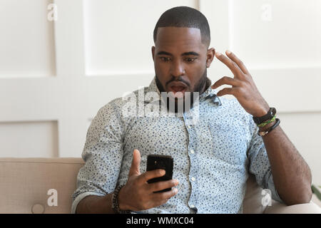Shocked millennial african american man holding phone.