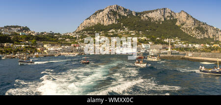 ISLE OF CAPRI, ITALY - AUGUST 2019: Panoramic view of the port on the island of Capri. A ferrry is docked in the harbour and small boats are leaving. Stock Photo