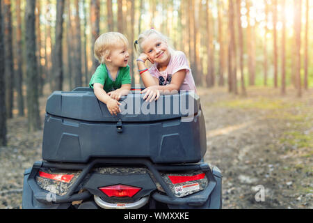 Cute adorable caucasian blond siblings having fun during atv 4x4 off-road adventure trip amog coniferous pine forest on brigh sunny day. Little boy Stock Photo