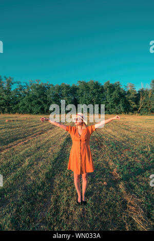 Young woman in orange dress with open arms in field Stock Photo