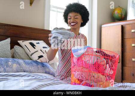 Smiling young woman doing laundry on bed Stock Photo