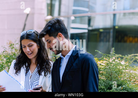 Preparing for meeting. Two young business people walking outside on the city street reading through documents Stock Photo