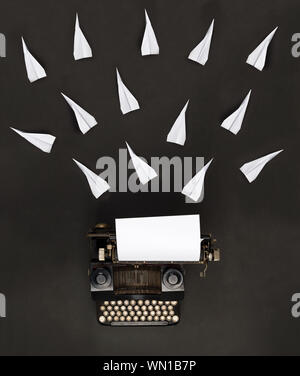 Paper planes flying from vintage retro typewriter on dark black background top view flat lay from above - journalism, creativity or writer concept