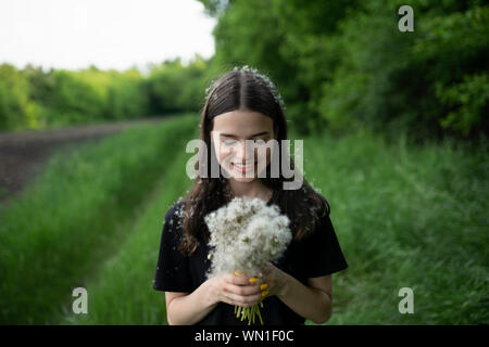 Smiling teenage girl holding dandelions in a field Stock Photo