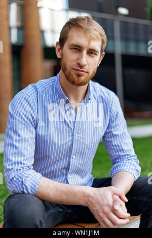 Man wearing striped shirt sitting on bench Stock Photo