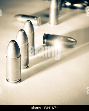 Three standing 9mm bullets alongside two fallen bullets with dramatic side light and sun-flare in warm tone black and white Stock Photo