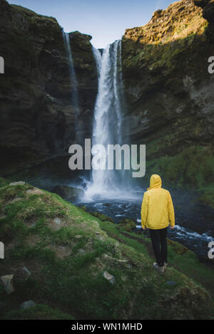 Man wearing yellow raincoat by Kvernufoss waterfall in Iceland Stock Photo